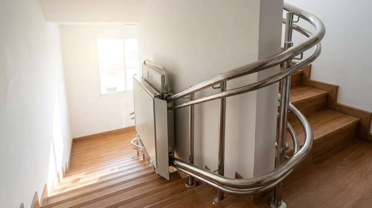 Montascale a pedana per carrozzina con binario curvilineo: piattaforma richiudibile contro la parete su una scala con pianerottolo intermedio
